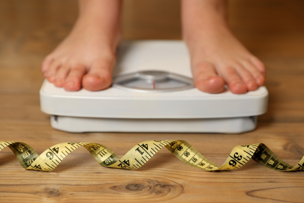 feet standing on floor scale with measuring tape in foreground