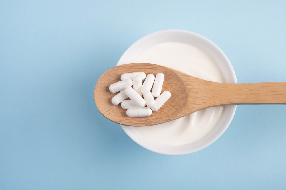 probiotic supplements on wooden spoon over bowl of yogurt